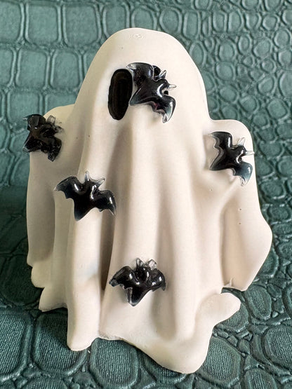 A white ghost-shaped Halloween decoration with black bat details, displayed on a textured dark green surface.