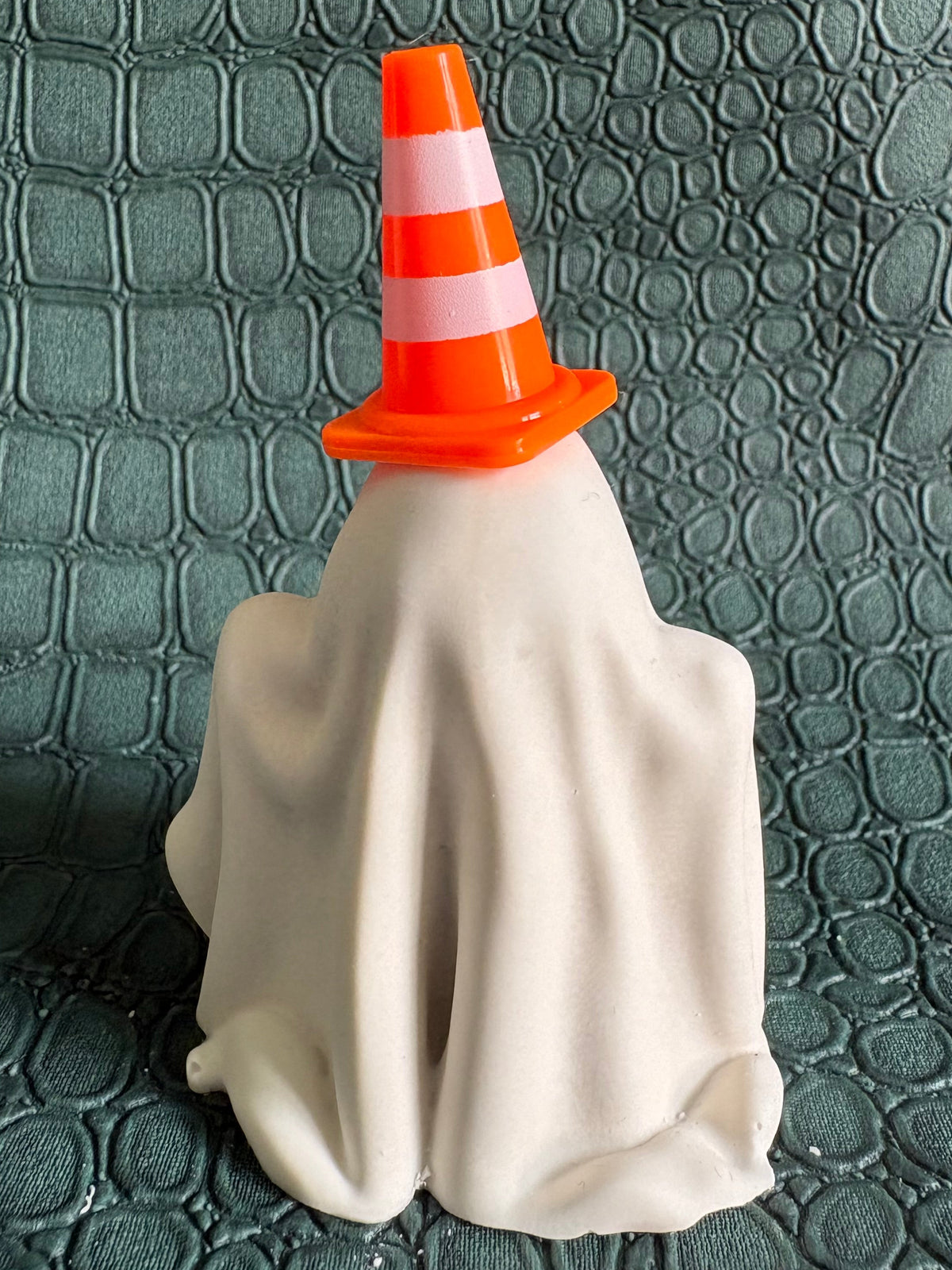 A ghost-shaped Halloween decoration covered in white fabric and wearing an orange traffic cone hat, set against a dark textured background.