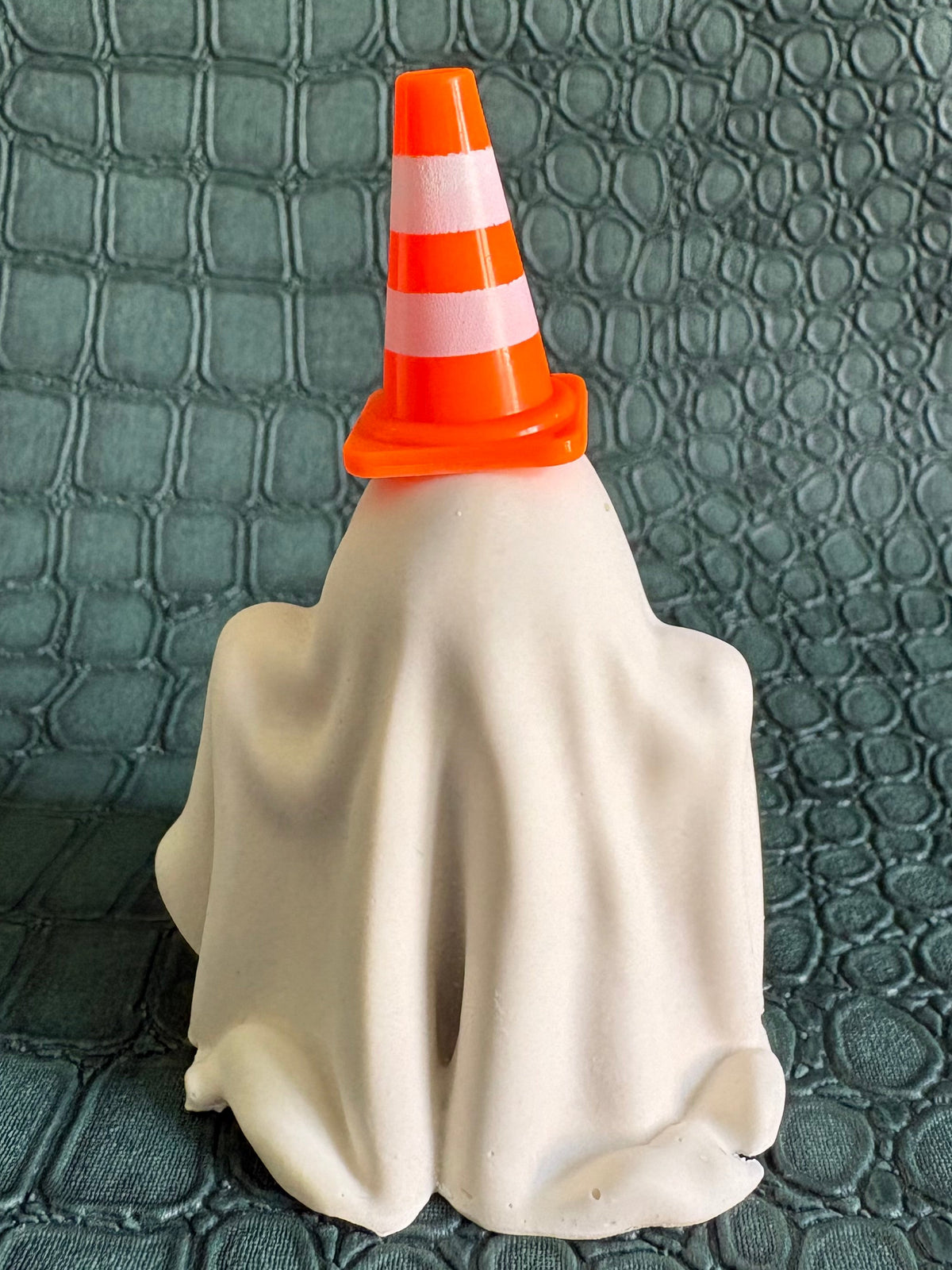 A Halloween ghost decoration covered in a white sheet and topped with an orange and white traffic cone, set against a dark textured background.