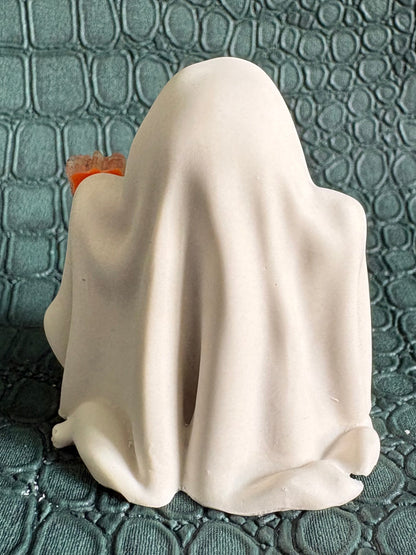 A small white ghost figurine draped in a sheet, standing on a textured dark teal surface.