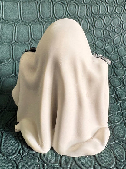 A small white fabric-covered object, possibly a plush toy or soft accessory, photographed from above on a textured dark green embossed surface.