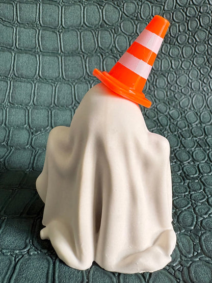 A Halloween decoration shaped like a ghost draped in a white sheet, wearing an orange and white striped traffic cone hat, set against a dark green textured crocodile-patterned background.